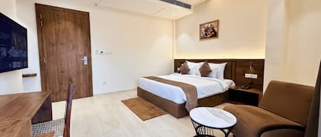 A modern hotel room with a large bed, a desk, a chair, and a small table.