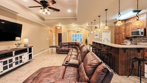 A spacious living room with a large leather sectional sofa, a flat-screen TV, and a ceiling fan. - Spacious 3BR Home • Sleeps 6 • Open Living • Private Yard (Victoria)