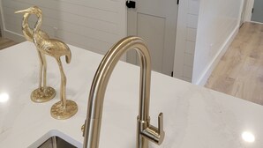 Eine moderne Küche mit weißer Arbeitsplatte, einem goldenen Wasserhahn und einer dekorativen, goldenen Vogel-Skulptur.
