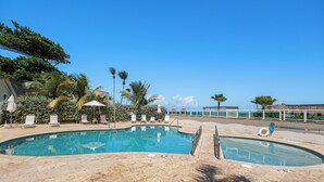 A swimming pool with lounge chairs and umbrellas, surrounded by palm trees and a clear blue sky. - Beachfront Luxury Studio Viejo San Juan (San Juan)