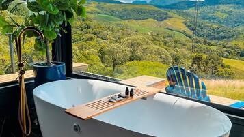 A modern bathroom with a freestanding bathtub, a wooden tray, and a potted plant.