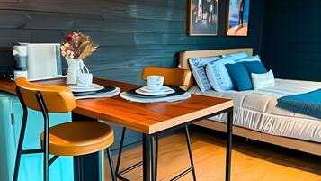 A modern room with a wooden dining table, two chairs, a sofa, and a bed. There are wall-mounted lights, a security camera, and artwork on the walls.