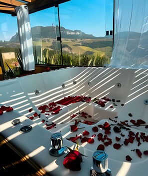A large bathtub with rose petals, a glass shower enclosure, and a scenic view of hills and buildings. - Refugio mirante da montanha (Alfredo Wagner)