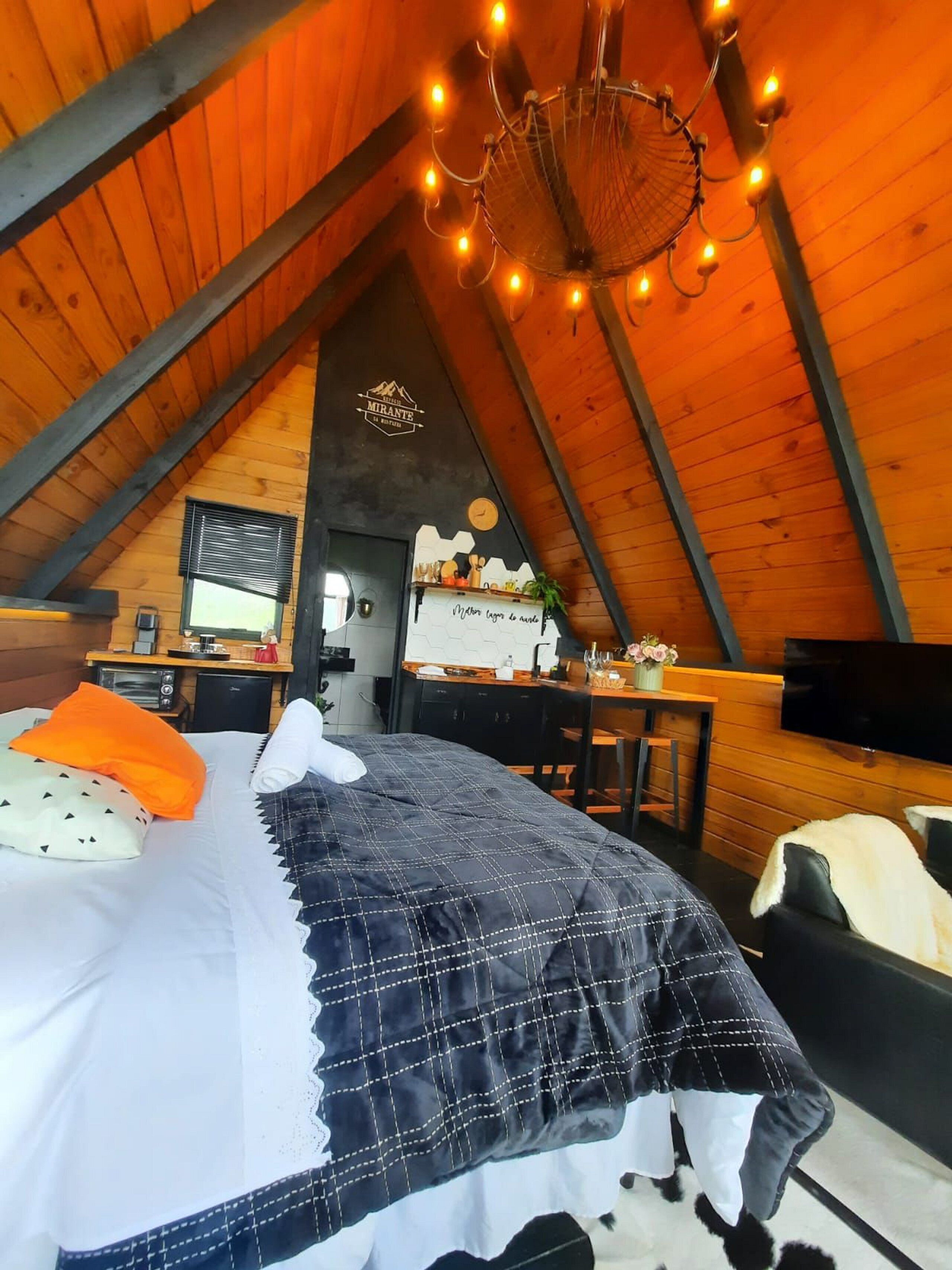 Een gezellig slaapkamer op zolder met een bed, een bureau, een televisie en een kroonluchter.