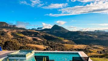 A pool with two chairs, surrounded by plants, overlooking a mountainous landscape.