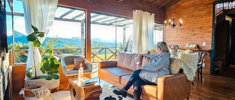 Un salón acogedor con techo de madera, sofá de cuero y un amplio ventanal con vistas a la montaña.