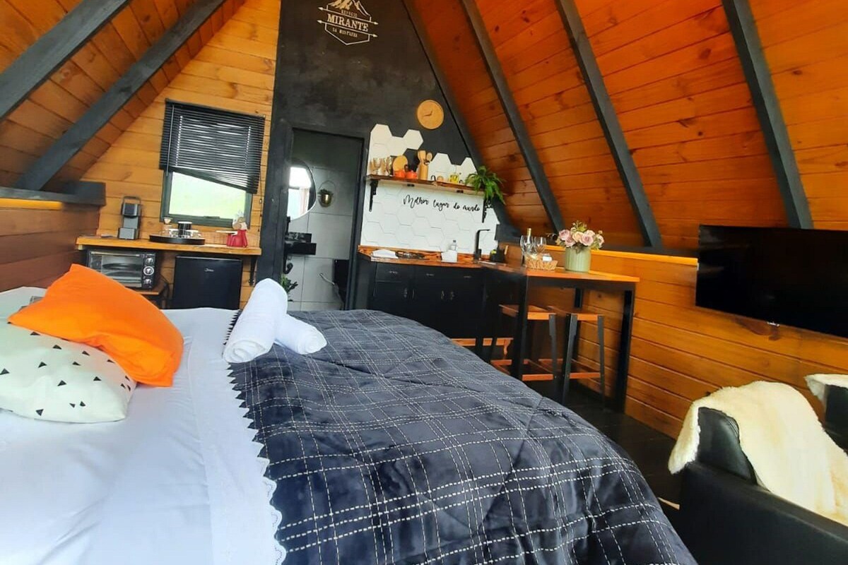 A cozy attic bedroom with a bed, a desk, a TV, and a chandelier.