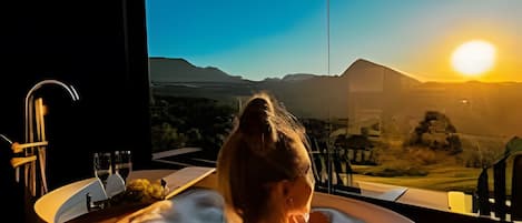 A woman in a bathtub with a view of mountains and a sunset.