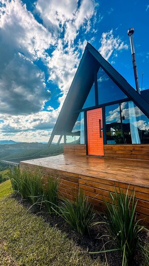 Un edificio moderno con terraza de madera, una puerta roja y vistas al paisaje.