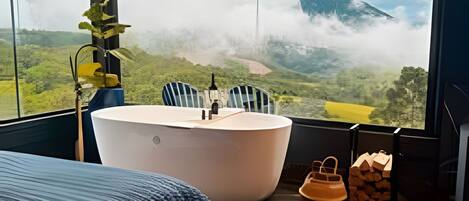 Un dormitorio con un ventanal grande, una cama, una bañera y vistas a un paisaje montañoso.