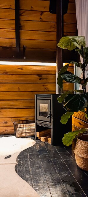 Ein Holzinterieur mit einem Metallfenster, einer Topfpflanze und einem schwarzen Gegenstand auf dem Boden.