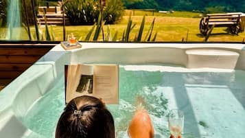 Iemand in een jacuzzi met uitzicht op een berg, met een glas in de hand.
