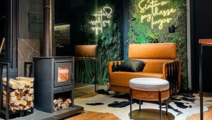 Ein gemütliches Wohnzimmer mit Kaminofen, einer bequemen orangefarbenen Couch und einem Neonlicht an der Wand.
