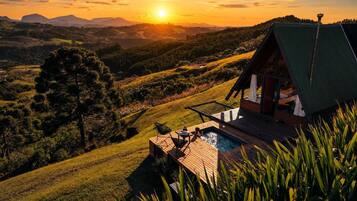 Una cabaña con piscina, rodeada de colinas y vista al atardecer.