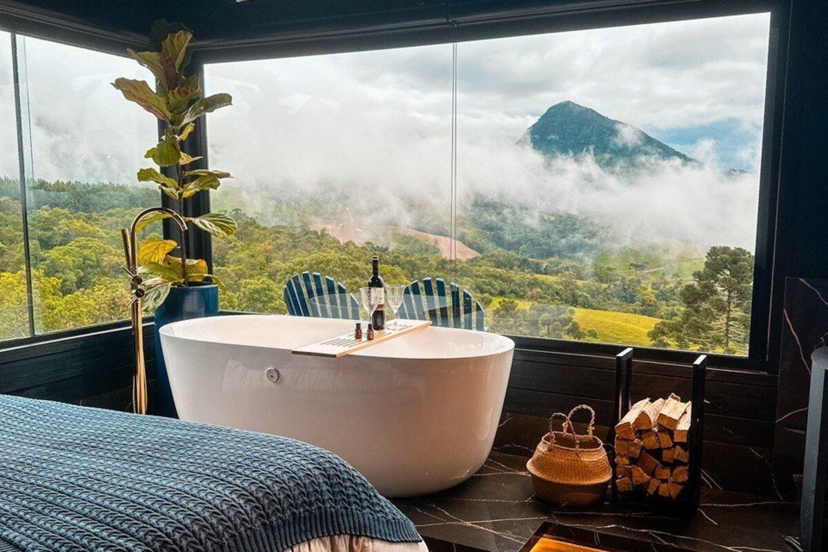 Un dormitorio con un ventanal grande, una bañera, una cama y una planta.