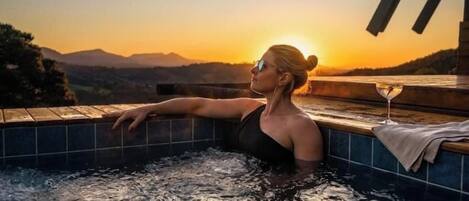 Una persona relajándose en un jacuzzi con vista al atardecer.