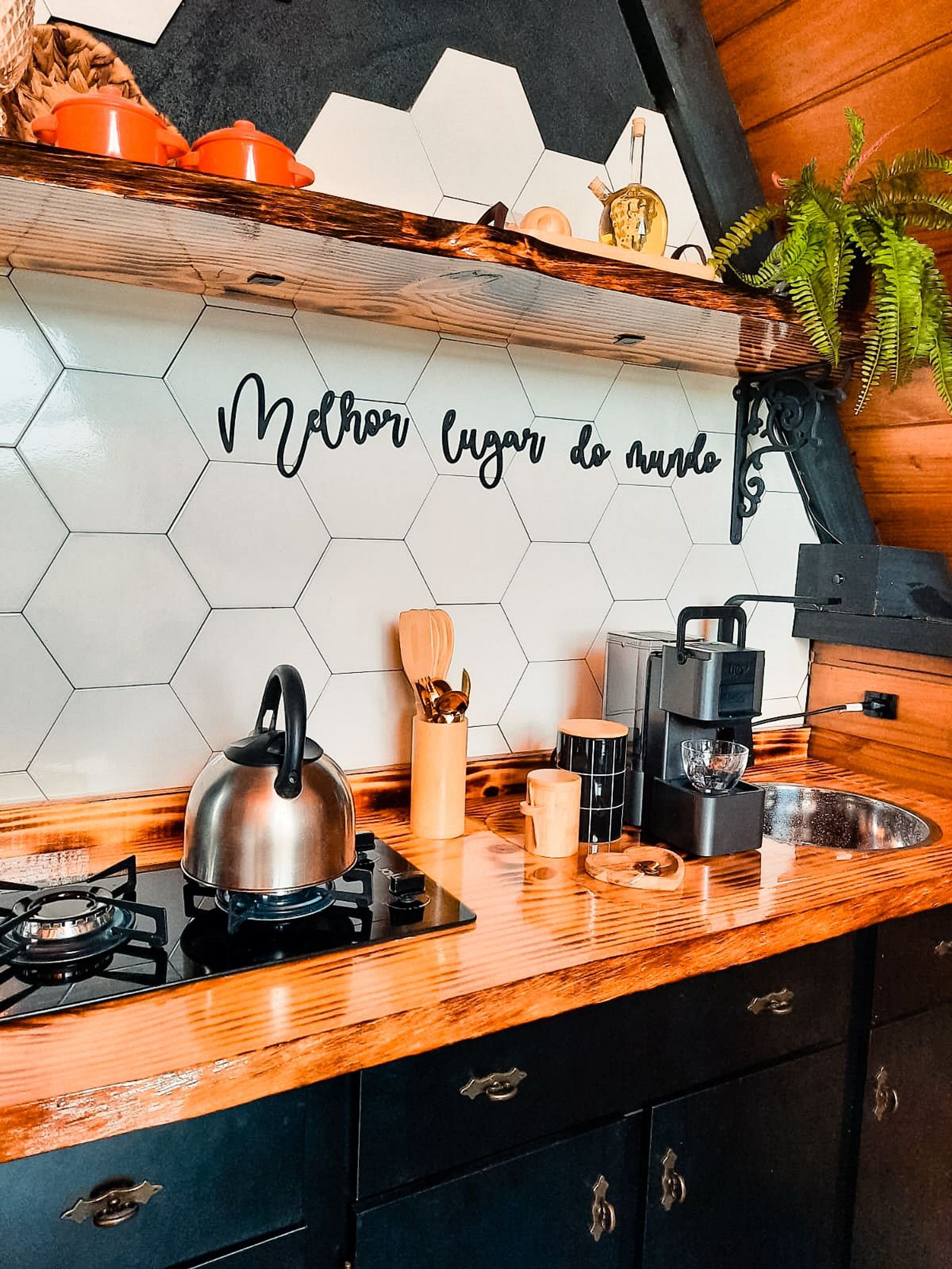 Une cuisine équipée d’une cuisinière à gaz, d’une bouilloire, d’une machine à café et d’un dosseret en carreaux hexagonaux orné d’une citation inspirante.