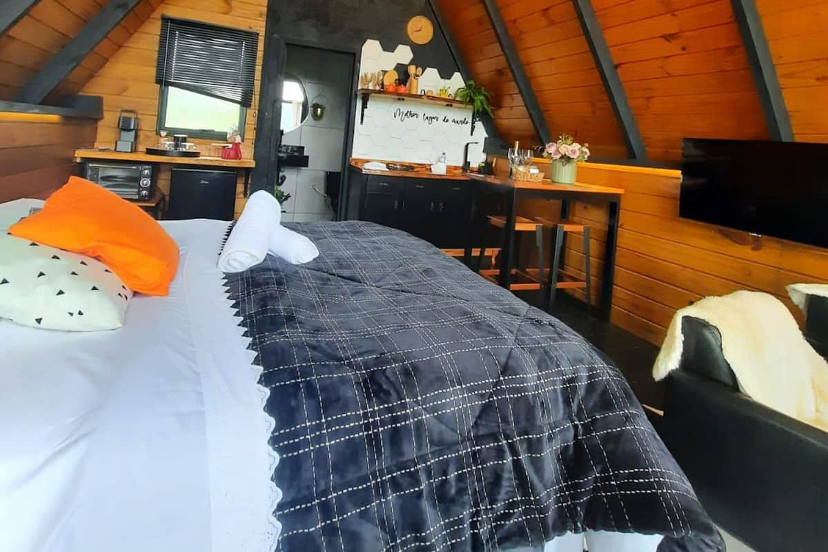 A cozy attic bedroom with a bed, a desk, a TV, and a chandelier.