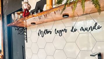 A kitchen with a wooden countertop, a stainless steel sink, a hexagonal tile backsplash with a phrase, and a plant.