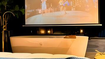 Ein Bett mit großem, darüber angebrachtem Fernseher, einem Nachttisch und einer Pflanze im Hintergrund.