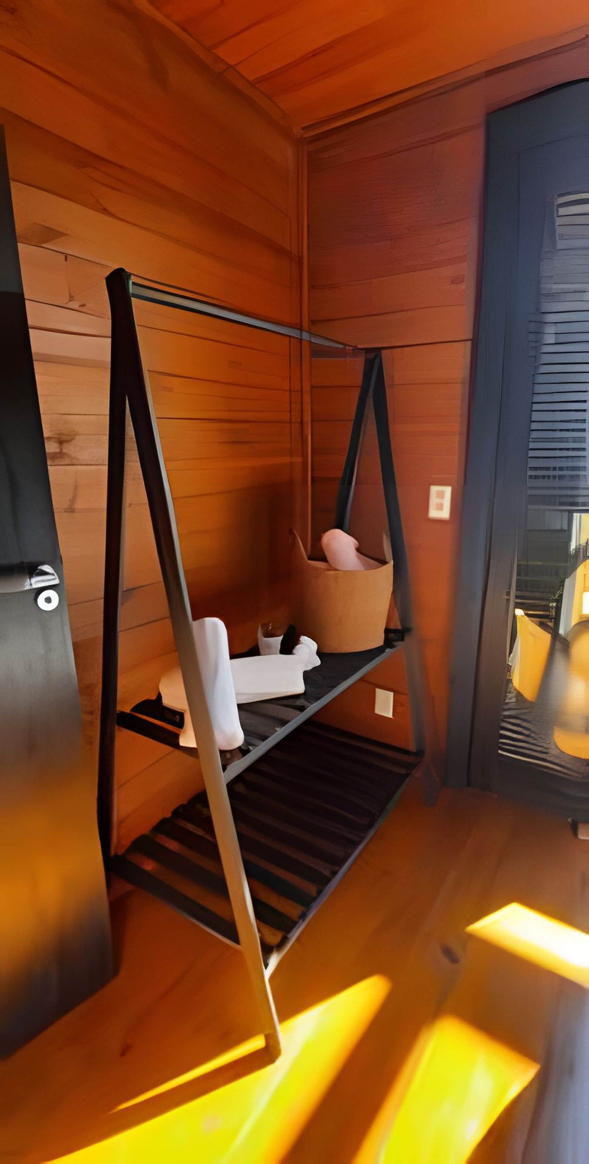 A wooden interior with a metal-framed bed, a hanging chair, and a small shelf with personal items.