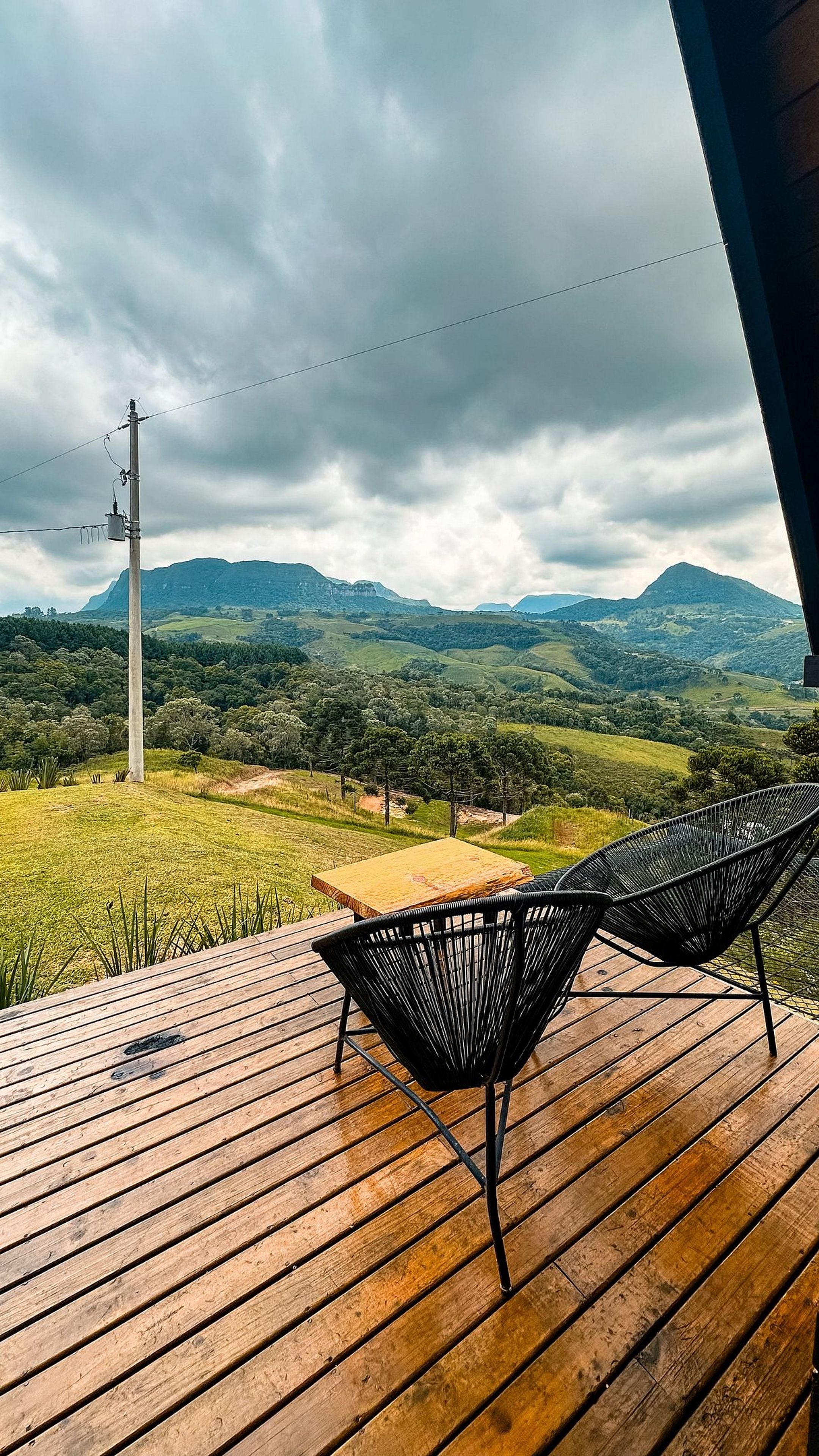 Eine Holzterrasse mit zwei schwarzen Stühlen, einem Tisch und Blick auf eine Berglandschaft.