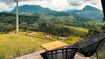 Eine Holzterrasse mit zwei schwarzen Stühlen, einem Tisch und Blick auf eine Berglandschaft.
