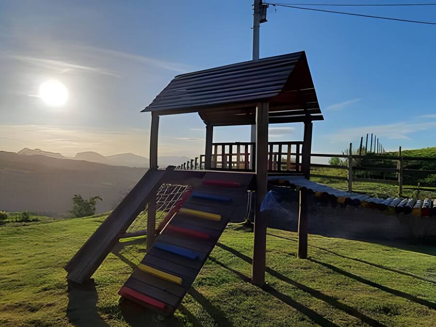 A playground with a slide and a small shelter, set against a backdrop of mountains and a clear sky.