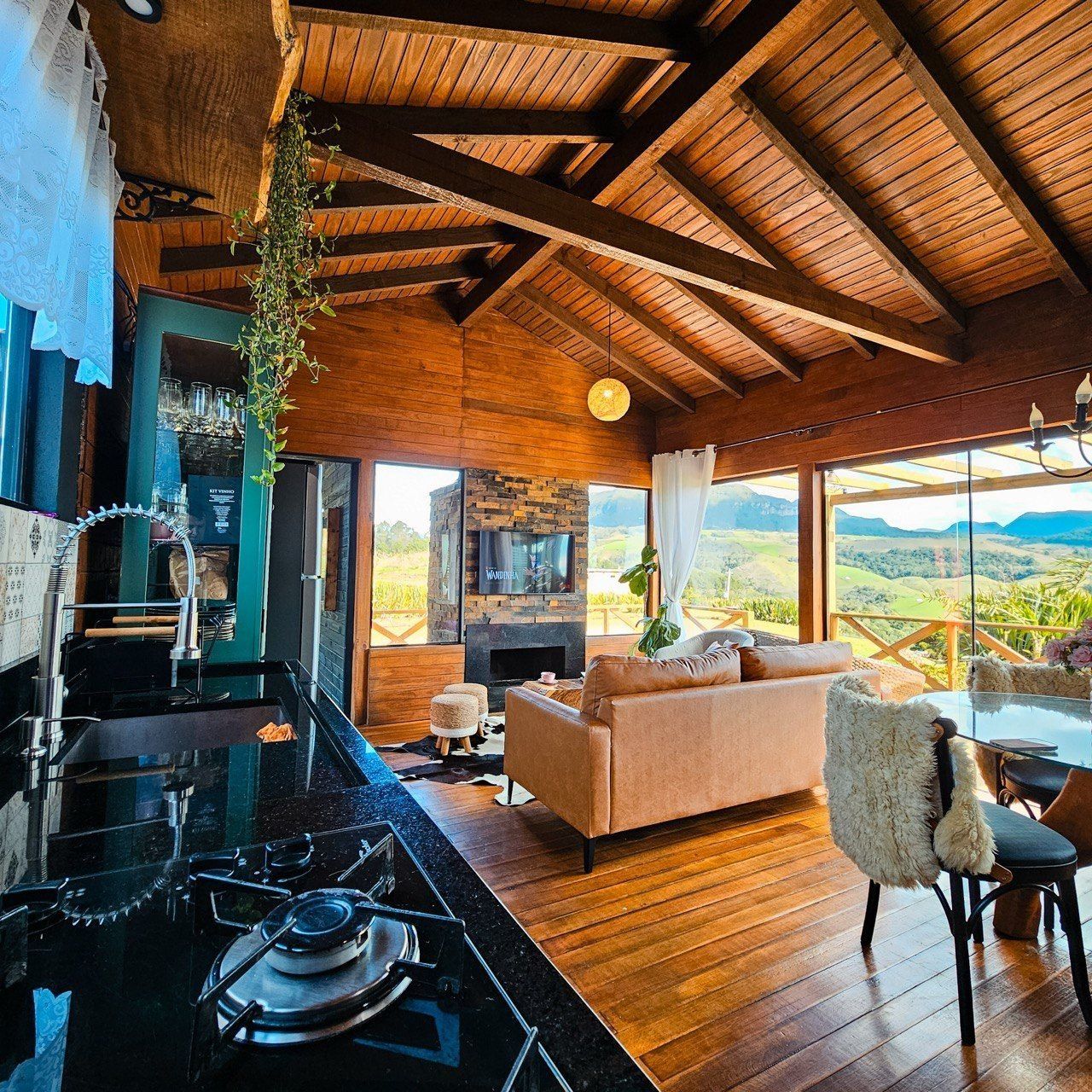 A modern kitchen with a gas stove, a stone fireplace, and a large window overlooking a scenic landscape.