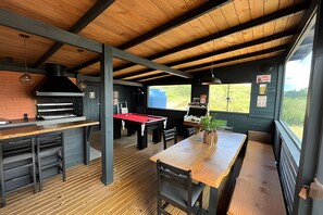 Un interior rústico con mesa de billar, barra y un ventanal con vistas a follaje.