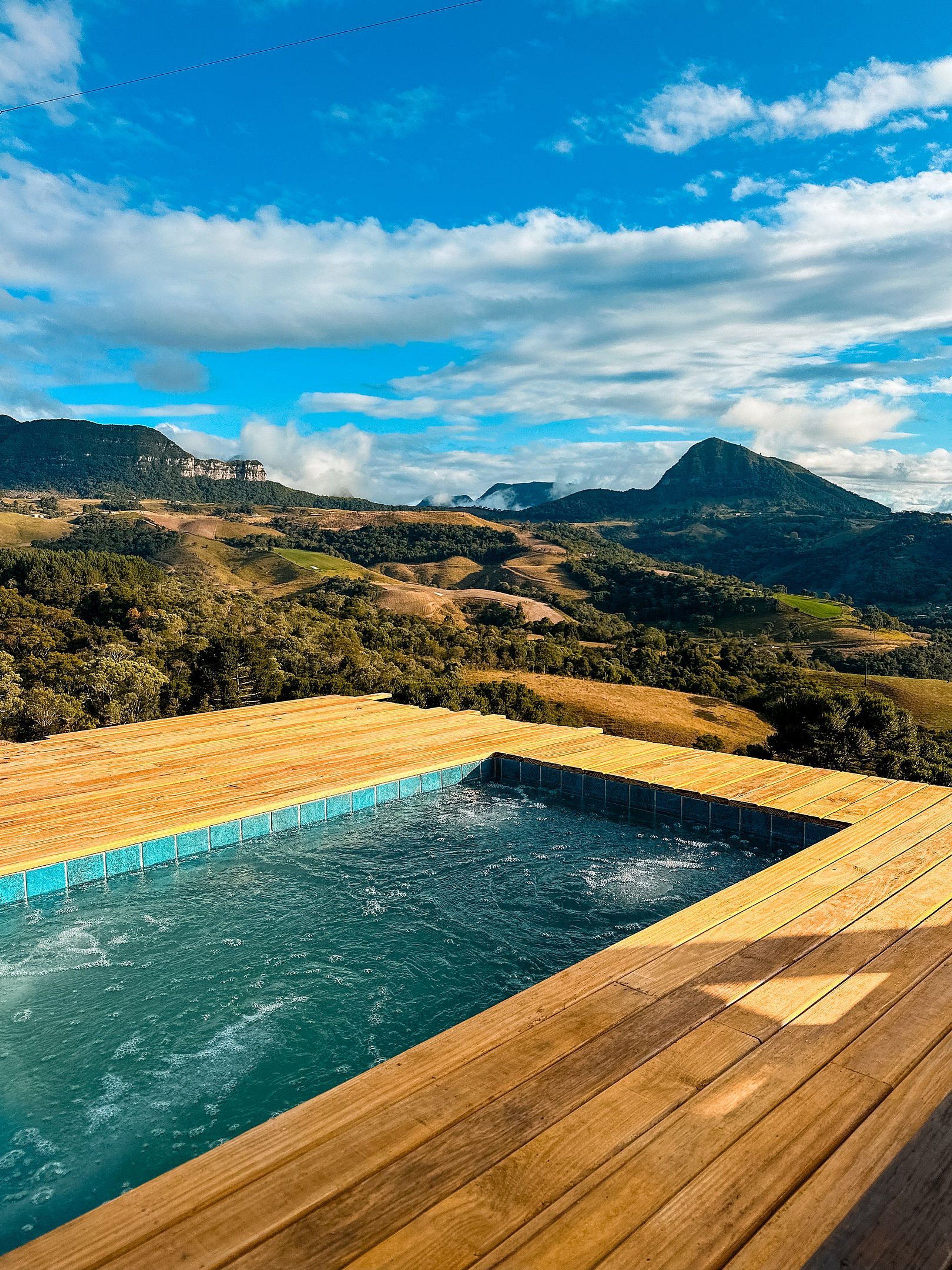 A wooden deck with a swimming pool, surrounded by a mountainous landscape.