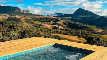 A wooden deck with a swimming pool, surrounded by a mountainous landscape.
