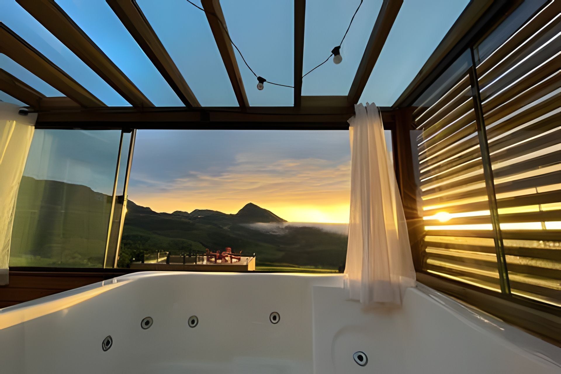 A room with a large window, a view of a mountain range, and a hot tub.