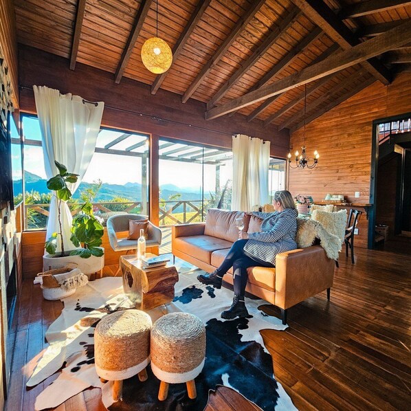 Un salón acogedor con techo de madera, sofá de cuero y un amplio ventanal con vistas a la montaña.