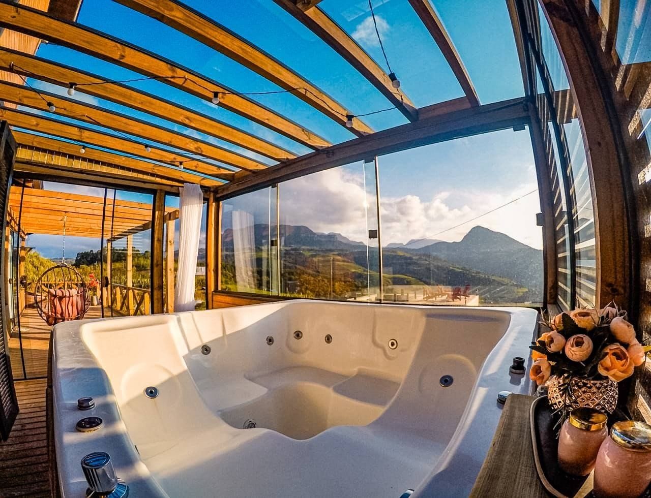 Un jacuzzi con terraza de madera y paredes de vidrio, con vista a montañas.