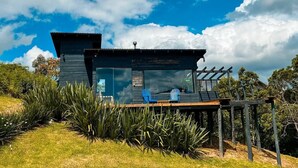 Une cabane moderne dotée d’une terrasse, de grandes fenêtres et d’une pergola.