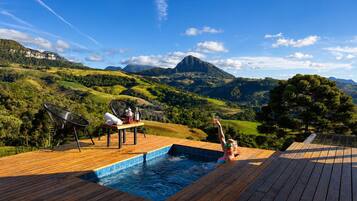 Eine Holzterrasse mit Whirlpool und Liegestühlen mit Blick auf eine gebirgige Landschaft.
