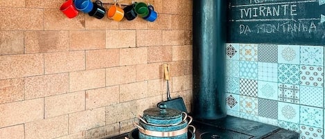 Una cocina rústica con un horno de leña, tazas de colores en un estante y una pizarra con escritura.