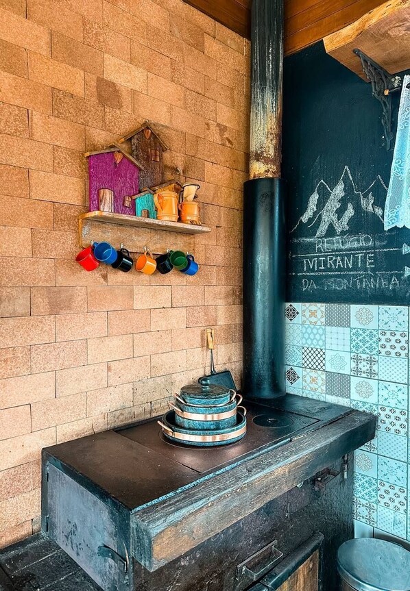 A rustic kitchen with a wood-burning stove, colorful mugs on a shelf, and a chalkboard with writing. - Refugio mirante da montanha (Alfredo Wagner)