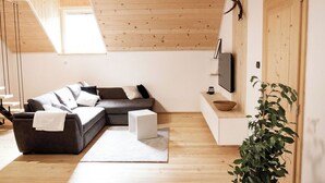Un salon moderne avec un plafond en bois, un canapé gris, un tapis blanc, un téléviseur et une plante.