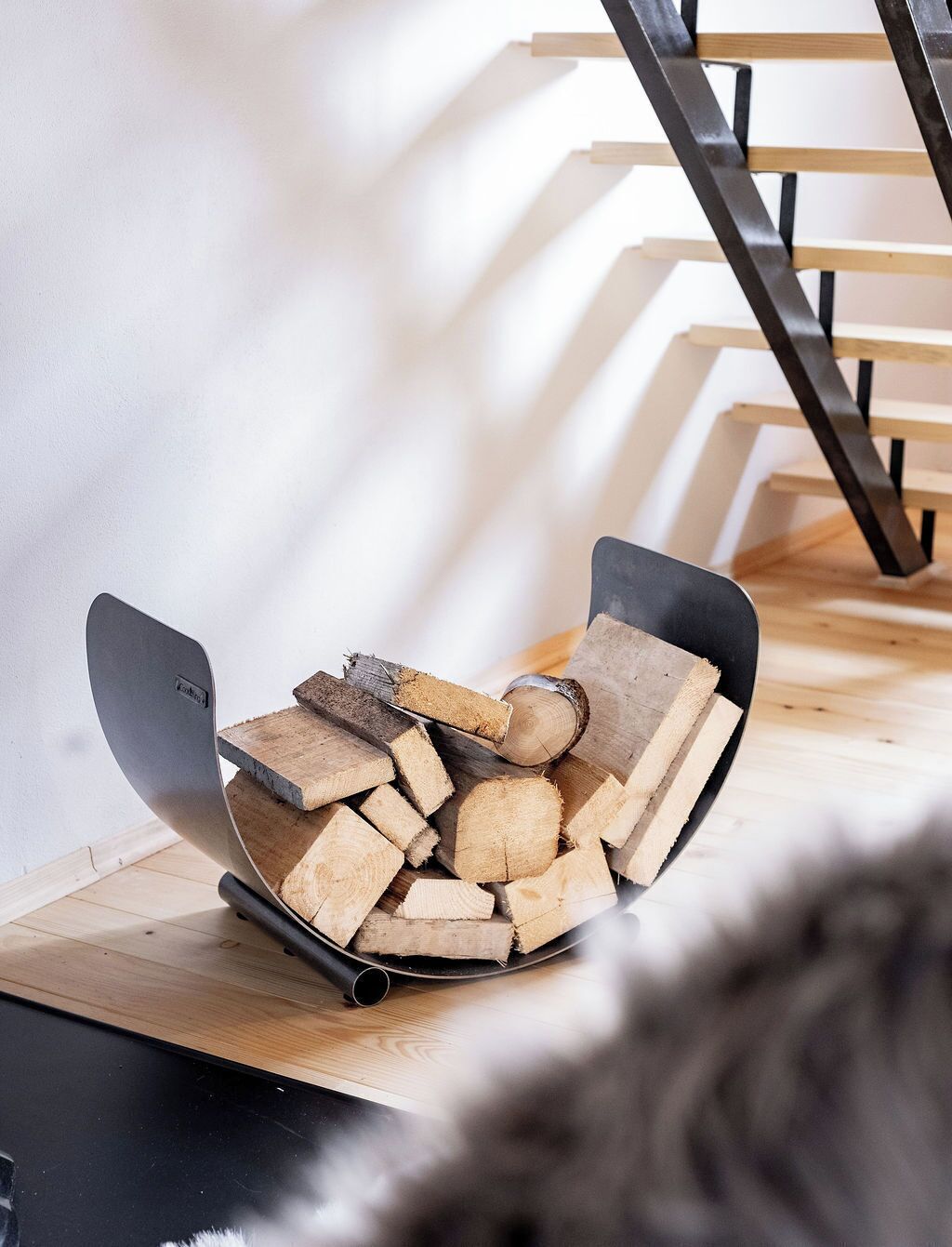 A fireplace with a modern design, a stack of firewood, and a metal chair.