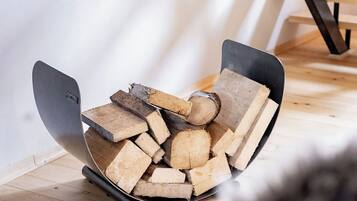 A fireplace with a modern design, a stack of firewood, and a metal chair.