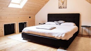 Une chambre avec un plafond en pente, un lit doté d’une tête de lit sombre, un puits de lumière et un tableau représentant un cerf.
