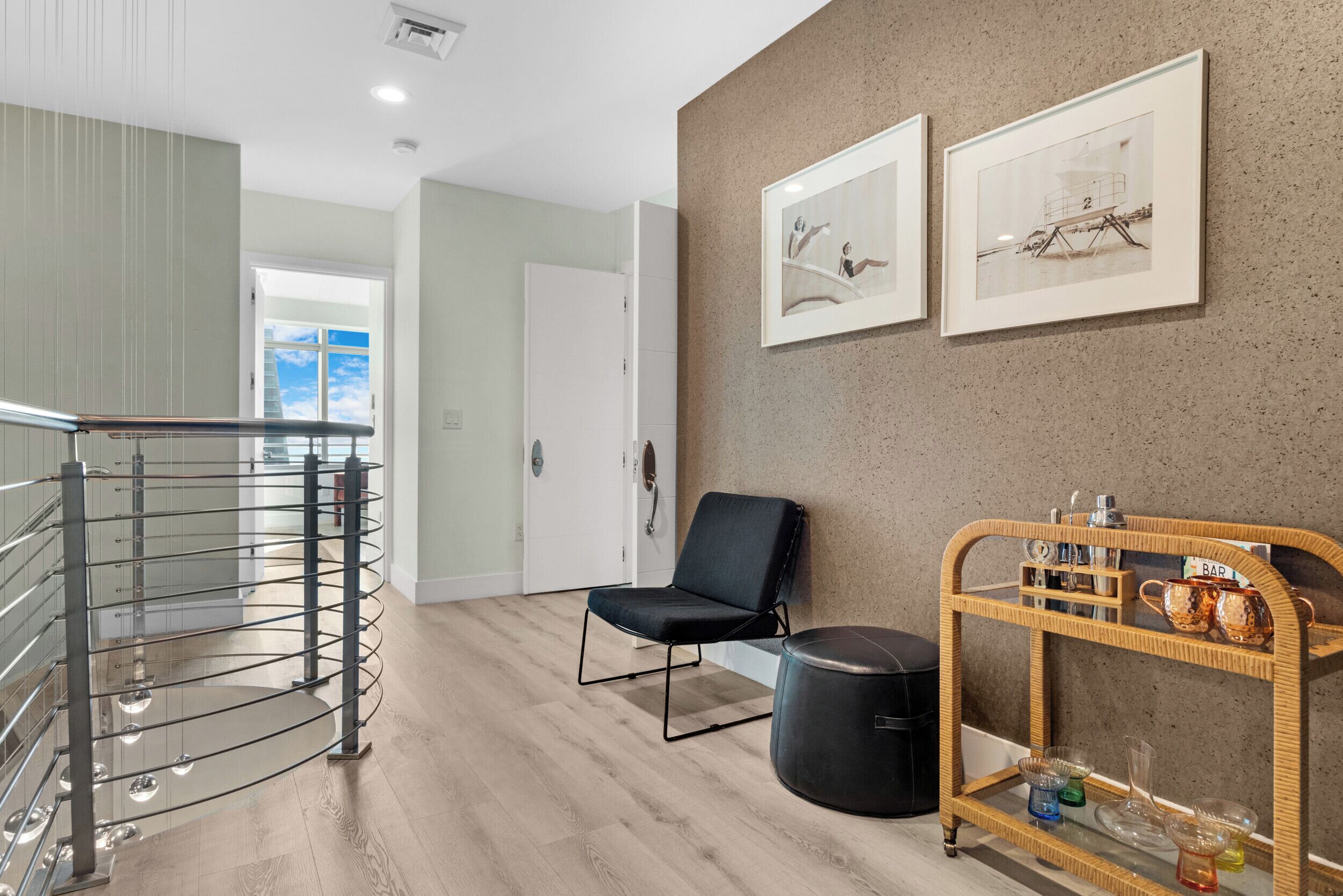 Ein modernes Interieur mit Treppe, einem schwarzen Stuhl, einem Korbtisch mit Barutensilien und gerahmten Kunstwerken an der Wand.