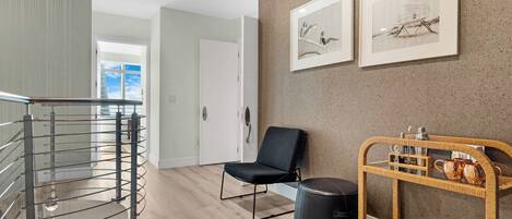 Ein modernes Interieur mit Treppe, einem schwarzen Stuhl, einem Korbtisch mit Barutensilien und gerahmten Kunstwerken an der Wand.