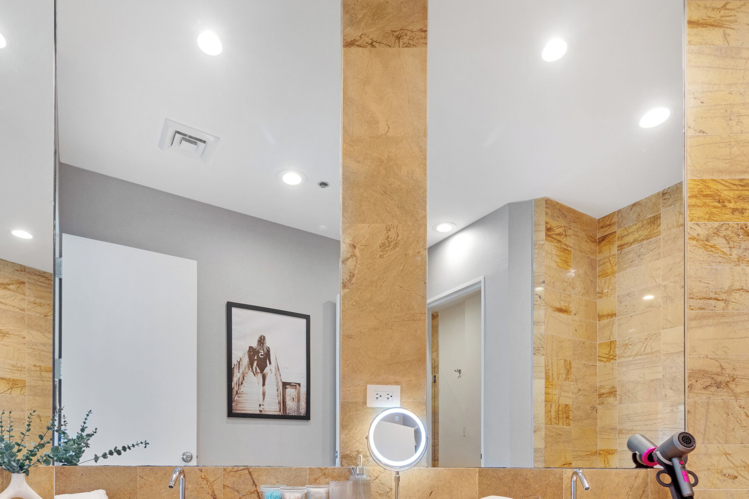 Un baño moderno con un espejo grande, paredes de mármol y un cuadro en la pared.