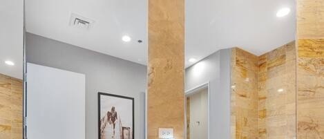 Un baño moderno con un espejo grande, paredes de mármol y un cuadro en la pared.