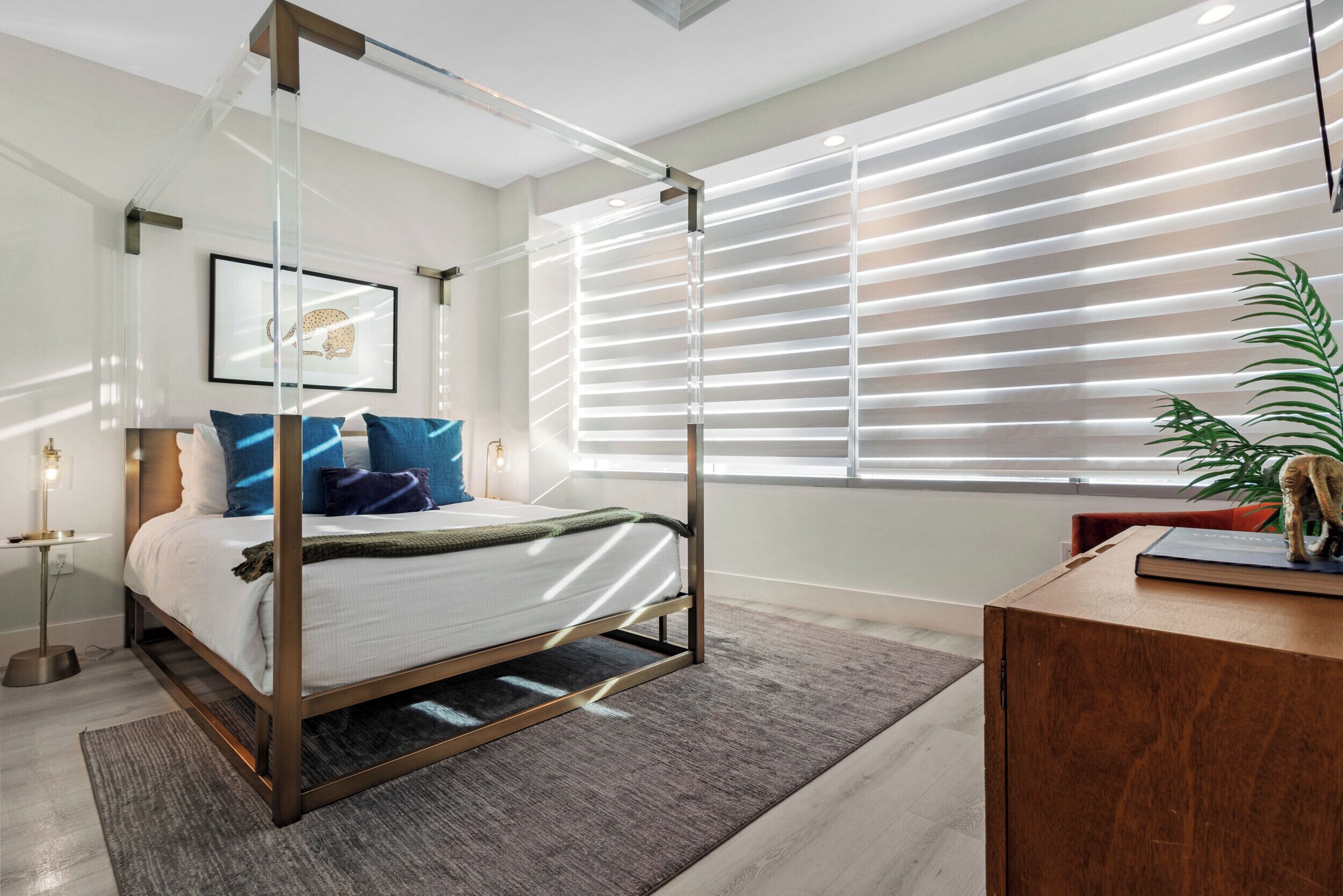 Ein modernes Schlafzimmer mit einem Himmelbett, einem Schreibtisch und einem großen Fenster mit Jalousien.