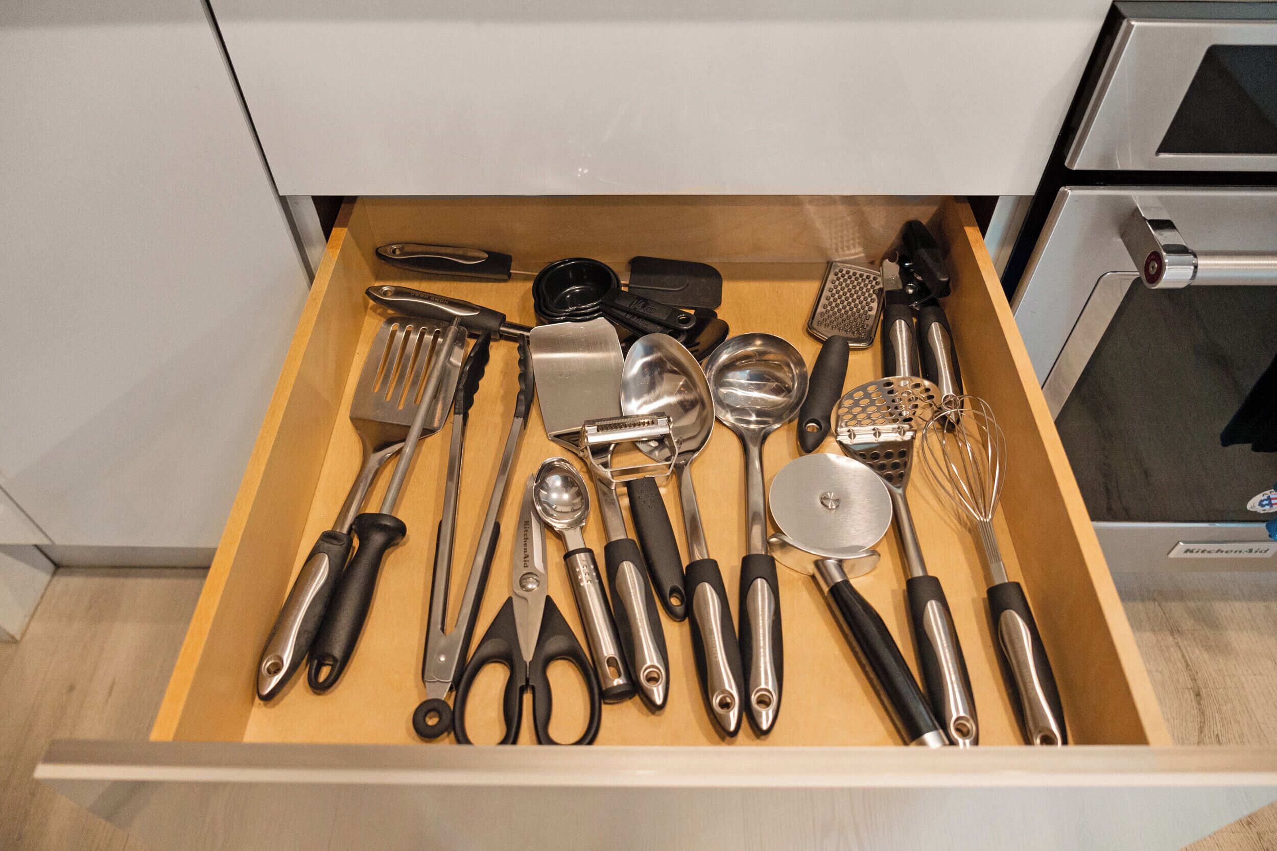 A drawer with various kitchen utensils including a grater, spatula, and whisk.