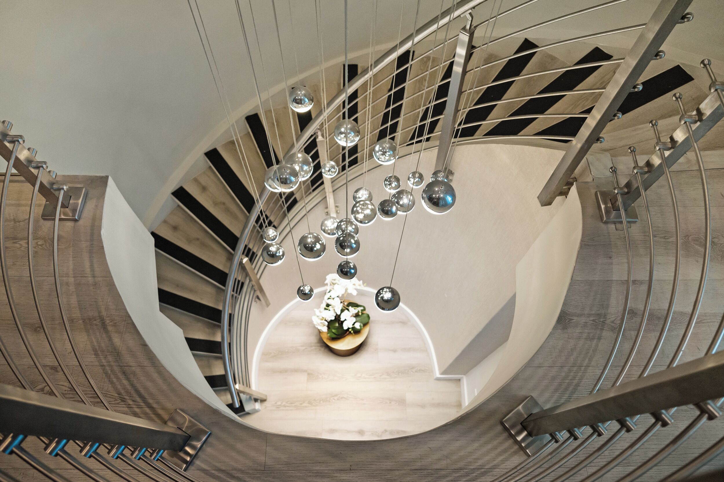 Una escalera de caracol con un arreglo floral en el centro, barandales de metal y espejos esféricos colgantes.